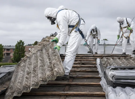 3 dakwerkers in witte pakken die asbest verwijderen op dak